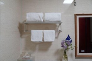 Un baño con dos toalleros que sostienen toallas blancas, un espejo enmarco y un florero con flores moradas.