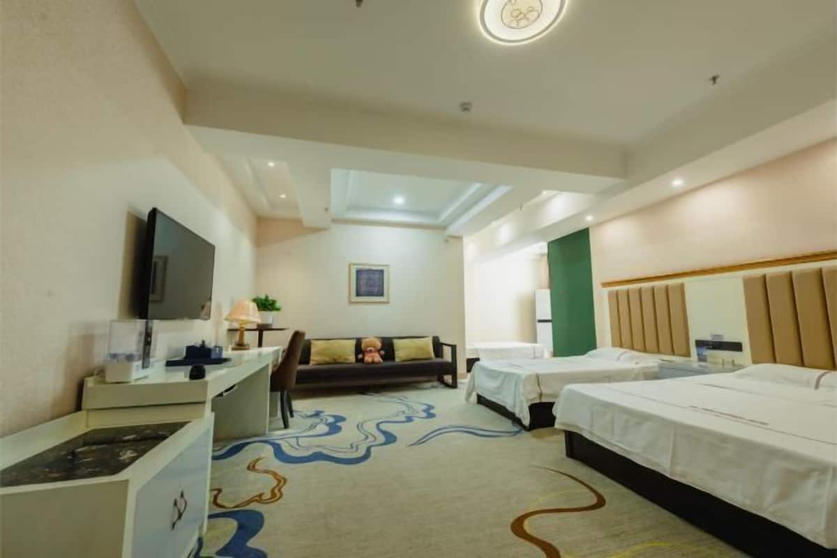 Ein Hotelzimmer mit Fernseher, einer Couch, zwei Betten, einem Schreibtisch und einem gemusterten Teppich.