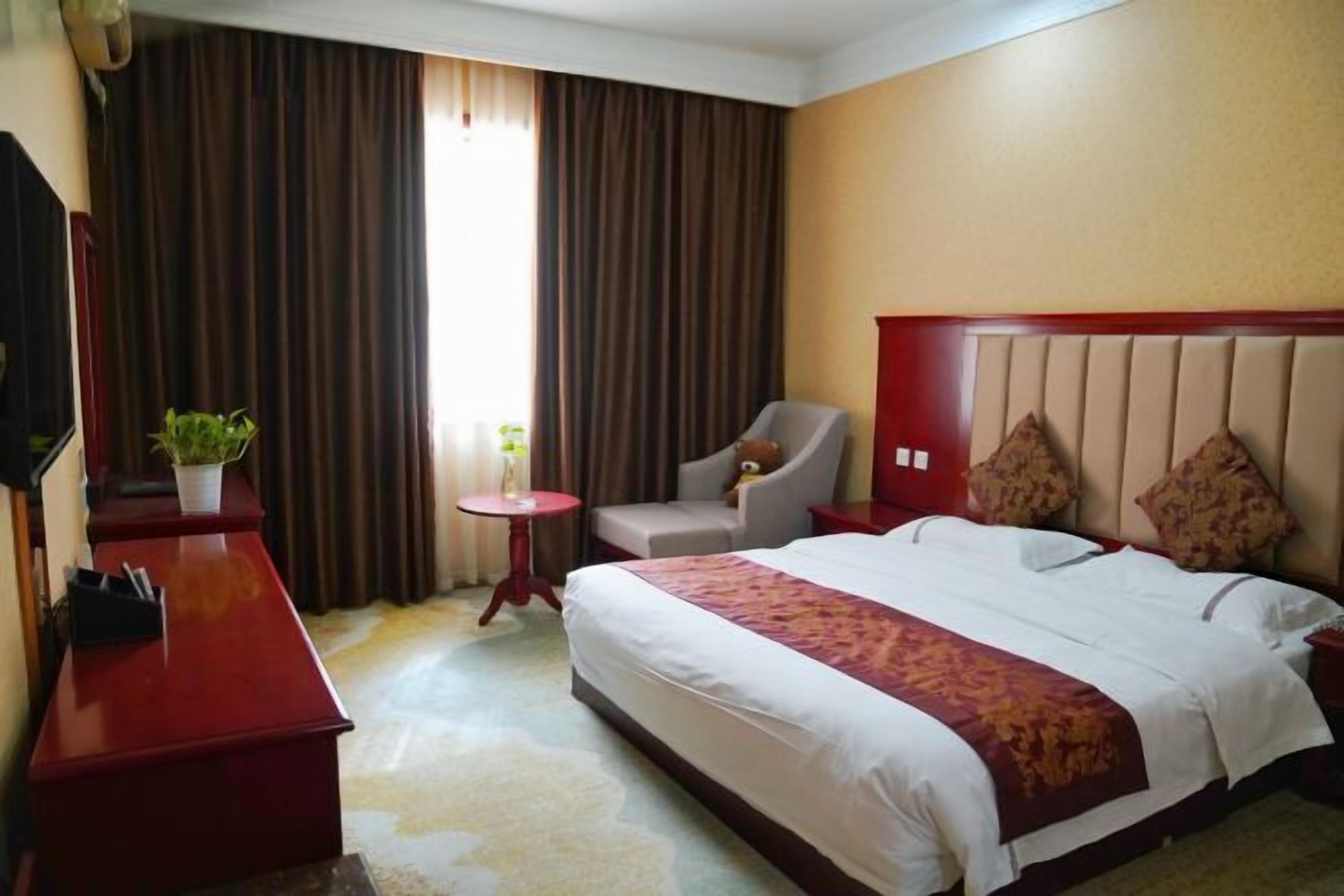 A hotel room with a large bed, a desk with a plant, a chair, and a small table.