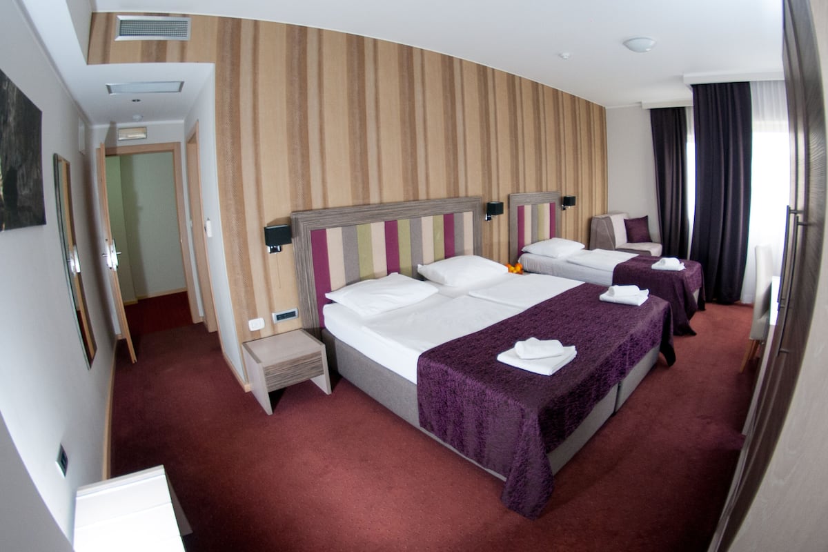 A hotel room with three beds, a wooden headboard, a red carpet, and a view of the corridor.