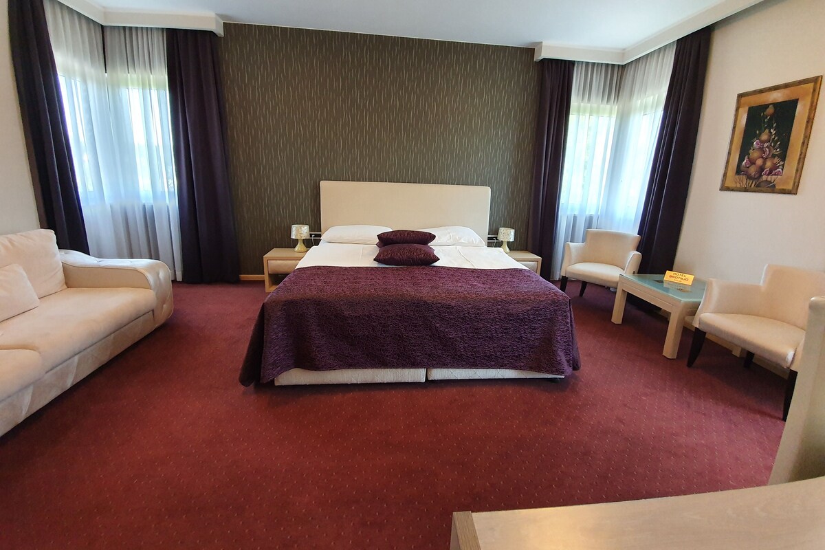 Habitación de hotel con una cama grande, dos mesitas de noche, un buró, un sofá, una silla y una pequeña mesa.