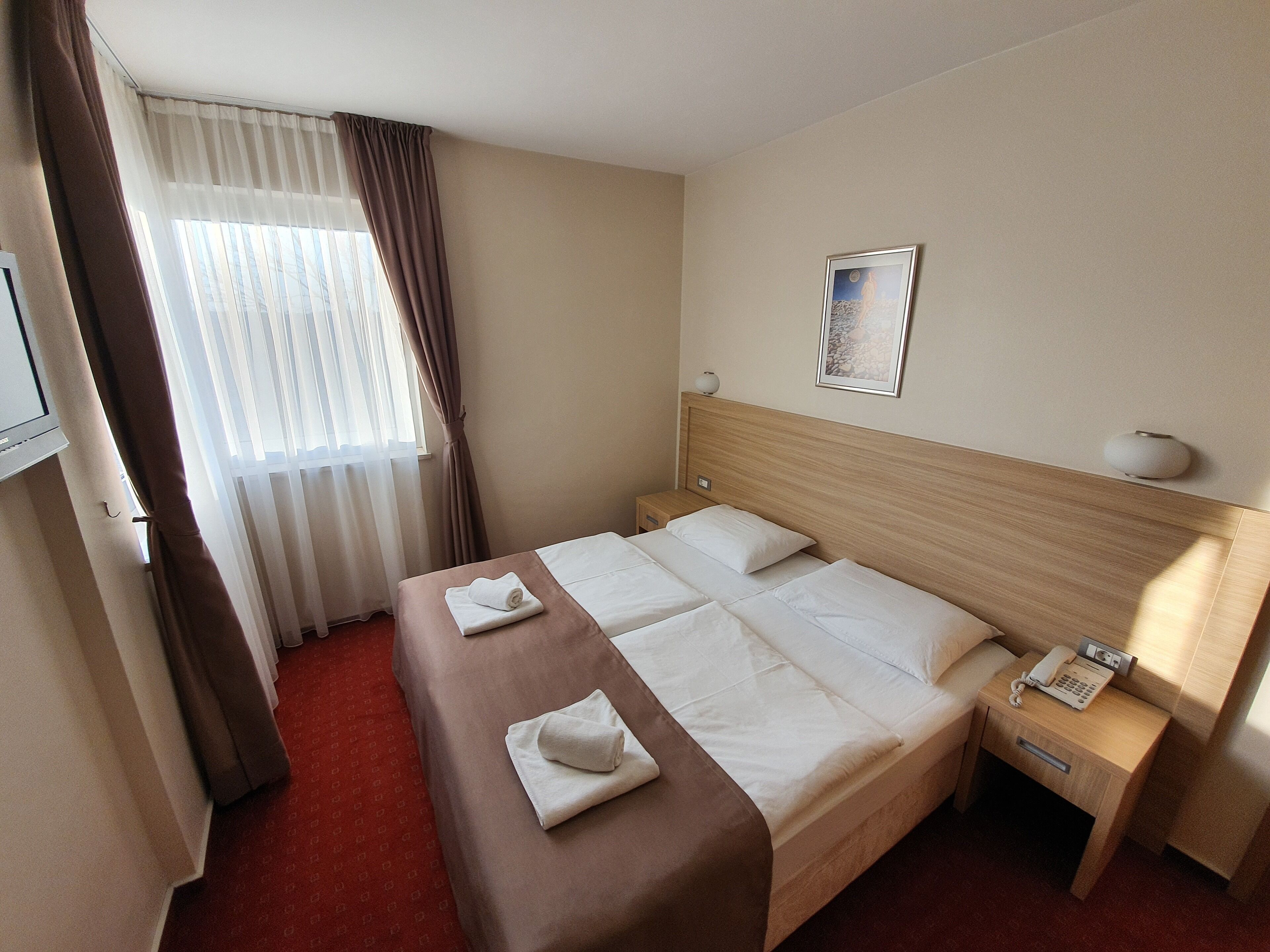 Une chambre d’hôtel avec un lit, une table de chevet avec une lampe, un téléphone et une fenêtre avec des rideaux.