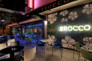 An outdoor dining area with tables and chairs, a wall with illuminated letters spelling 'BROCCO', and a neon sign above. - Brotnjo (Citluk)