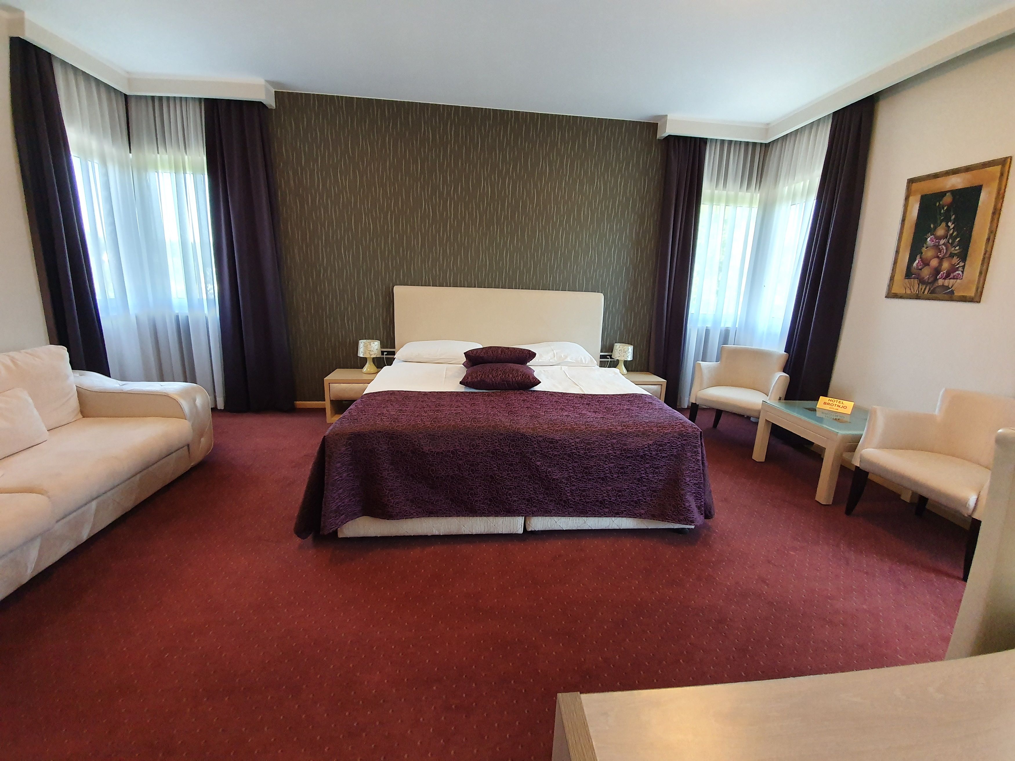 A hotel room with a large bed, two bedside tables, a nightstand, a sofa, a chair, and a small table.