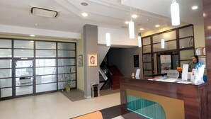 A hotel reception area with a glass door entrance, a reception desk, and a staircase leading to the upper floor. - Brotnjo (Citluk)