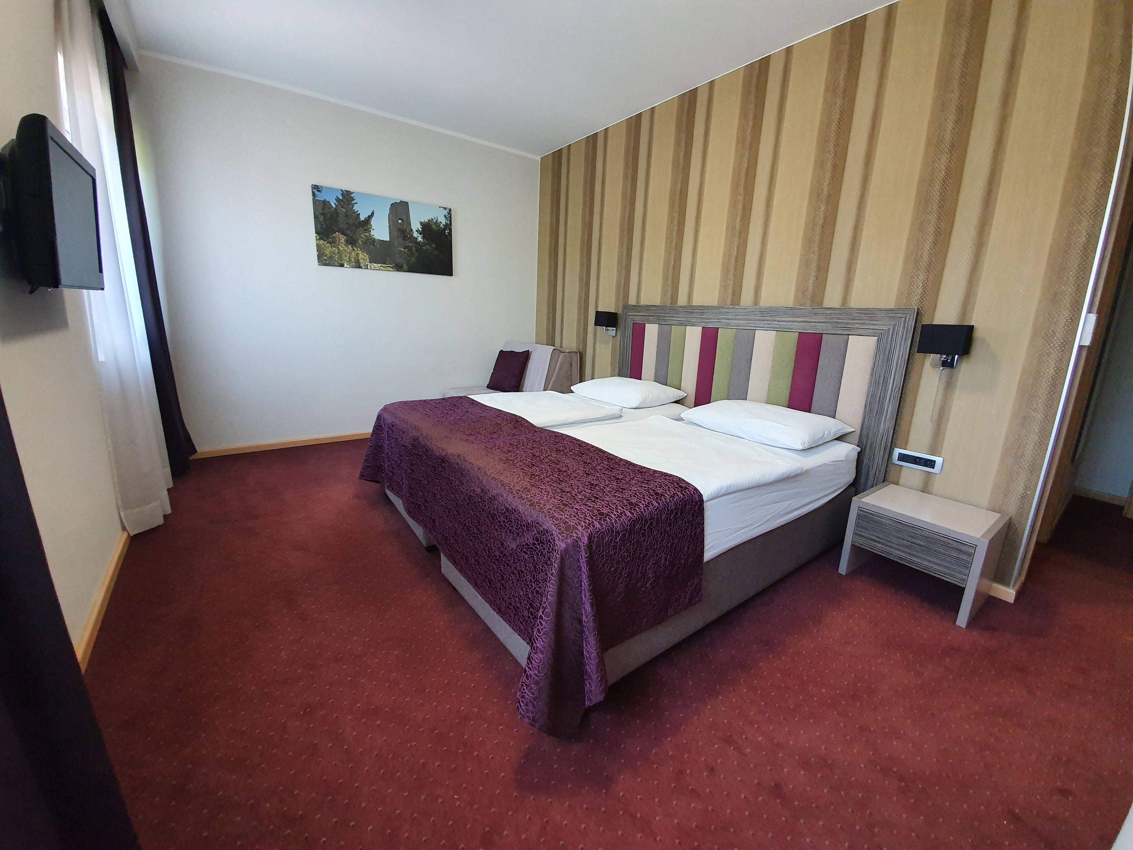 A hotel room with a bed, a bedside table, a wall-mounted TV, and a picture on the wall.