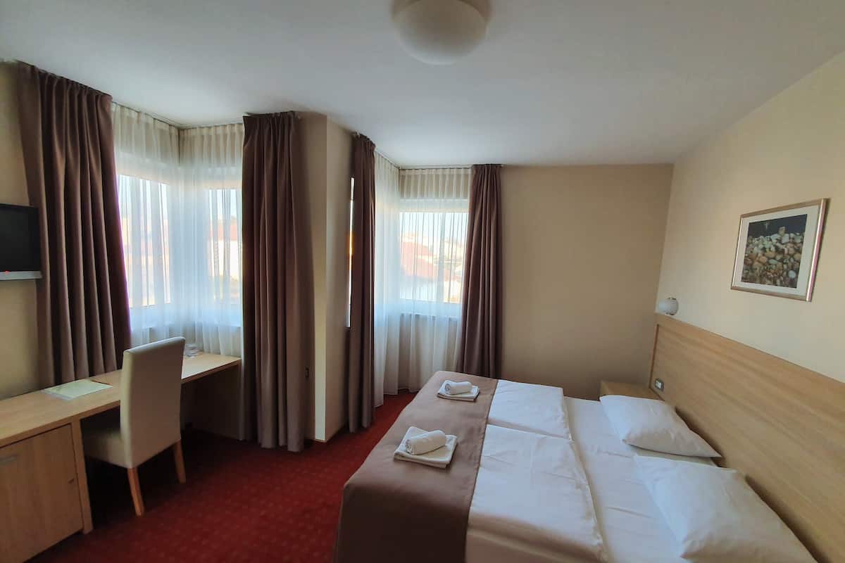 A hotel room with a bed, desk, chair, and a television.