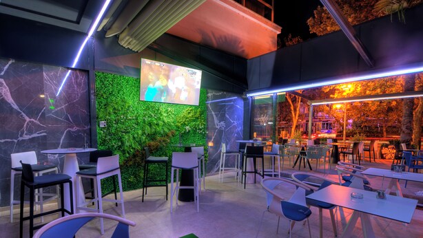 An indoor dining area with tables and chairs, a green wall with a screen, and a view of the outside. - Brotnjo (Citluk)