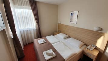 Quarto de hotel com cama, mesa de cabeceira com abajur, telefone e janela com cortinas.