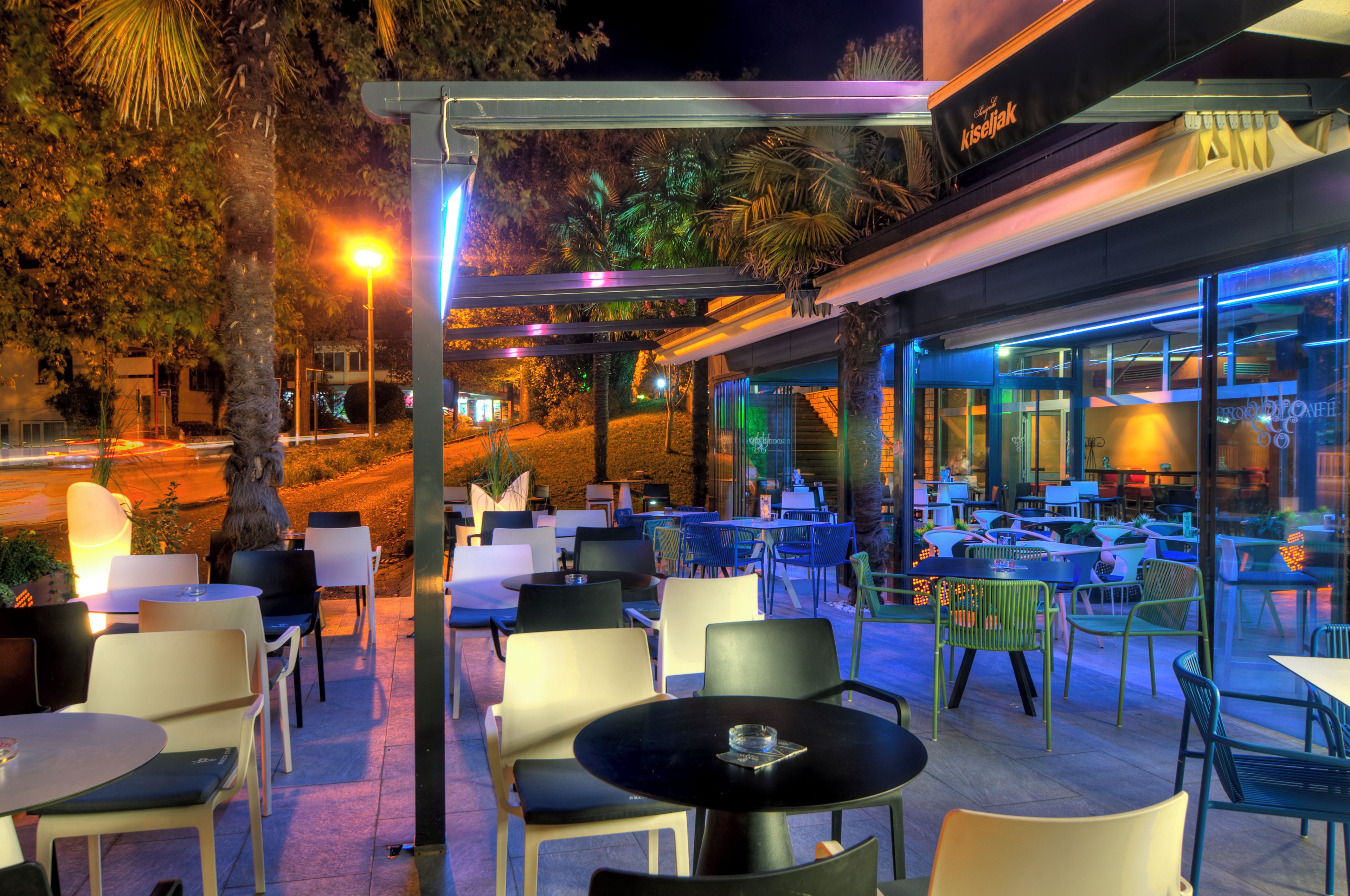 An outdoor cafe area with tables and chairs, a street view, and a building with glass windows.