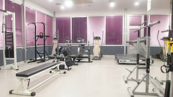 Uma academia com diversos equipamentos de exercícios, incluindo esteiras, aparelhos de musculação e um banco.