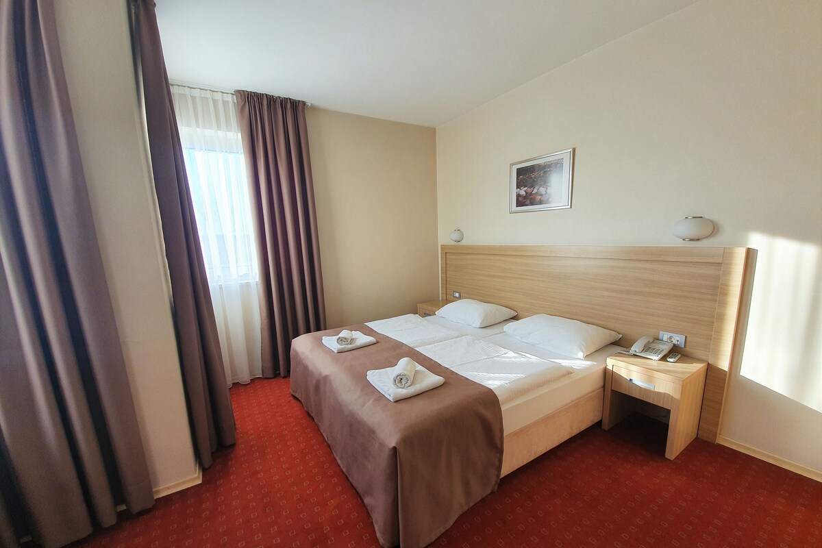 A hotel room with a large bed, a bedside table with a lamp, and a window with curtains.