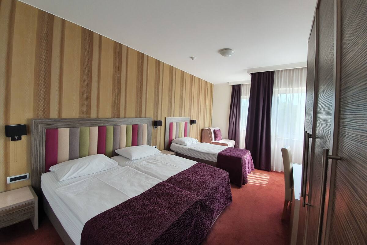 A hotel room with two beds, a large window with curtains, and a wooden headboard.