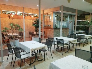 Un'area pranzo interna con tavoli e sedie, un muro in mattoni e piante in vaso.