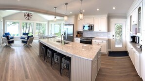 A spacious kitchen with a large island, white cabinetry, and a view of the outdoors. - Lakefront Getaway: The Blue Bungalow on Seneca Lake (Torrey)