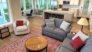 A modern kitchen with a central island, bar stools, and a dining area with a table and chairs. - Lakefront Getaway: The Blue Bungalow on Seneca Lake (Torrey)