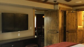 Une chambre à coucher avec un lit, un ventilateur de plafond, un téléviseur fixé au mur et des portes en bois.