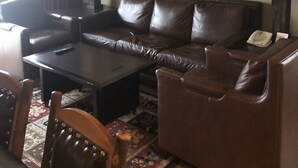 Un salon avec un canapé en cuir marron, une table basse et un lustre. Un tableau est accroché au mur et une lampe se trouve sur la table d’appoint.