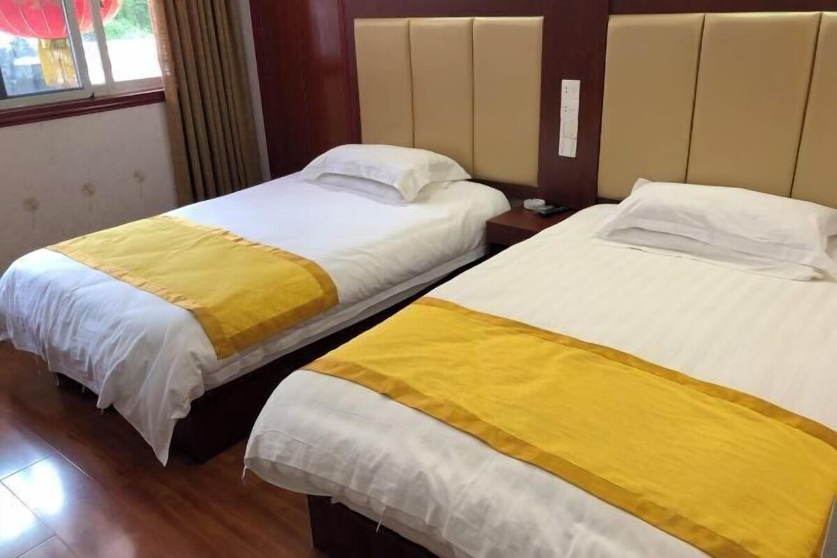 Dos camas individuales con cabeceros, piso de madera y una ventana con cortinas.
