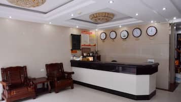 A reception area with a counter, two wooden chairs, a chandelier, and clocks on the wall.