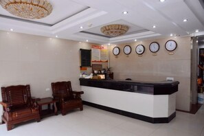 A reception area with a counter, two wooden chairs, a chandelier, and clocks on the wall. - Wudang Hotel (Danjiangkou)