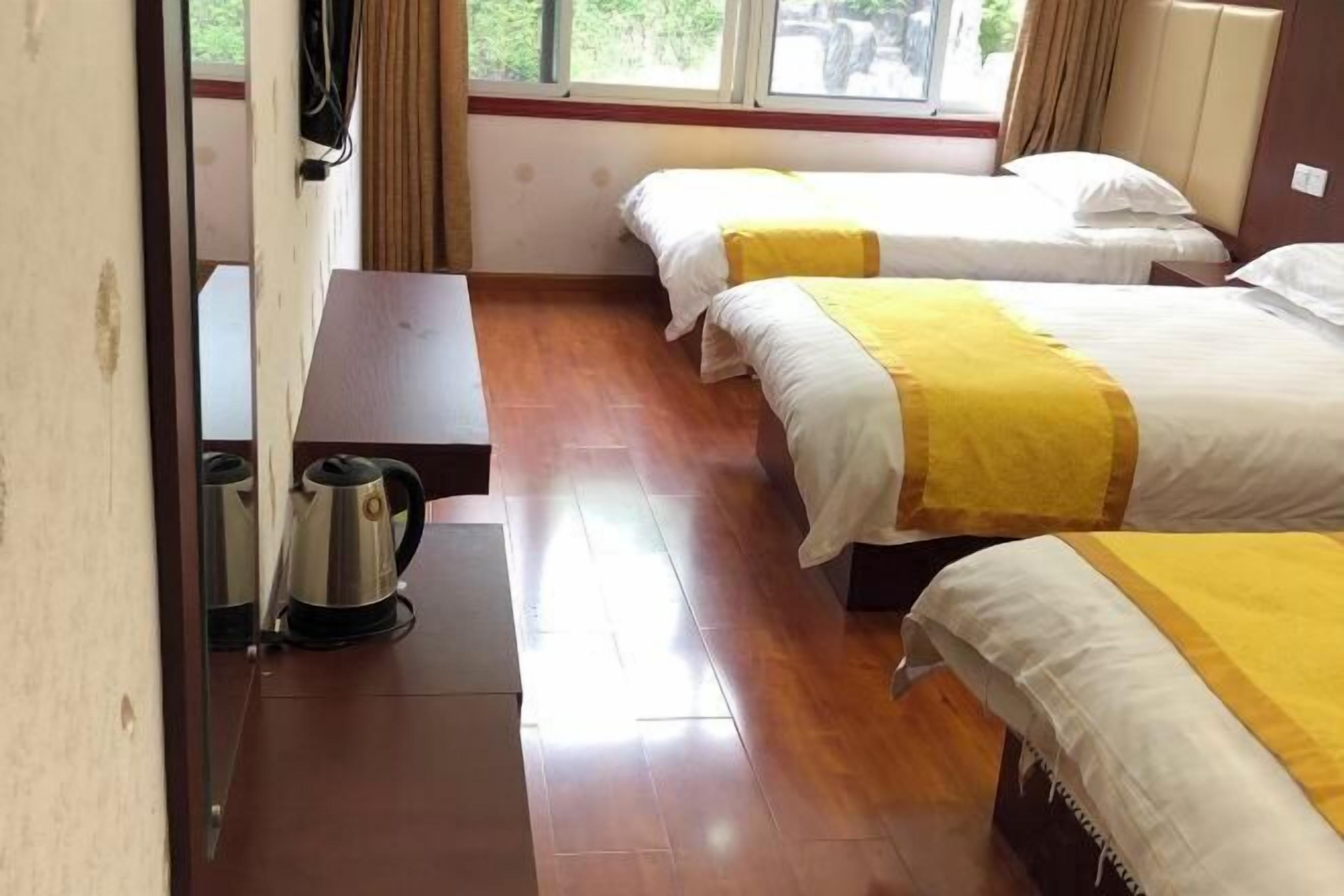A hotel room with two beds, a wooden floor, a small table with a kettle, and a window with curtains.