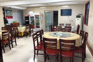 Un comedor con mesas y sillas redondas, un refrigerador y un televisor en la pared.