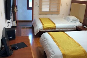 Habitación de hotel con dos camas, un escritorio con computadora y una ventana con persianas.