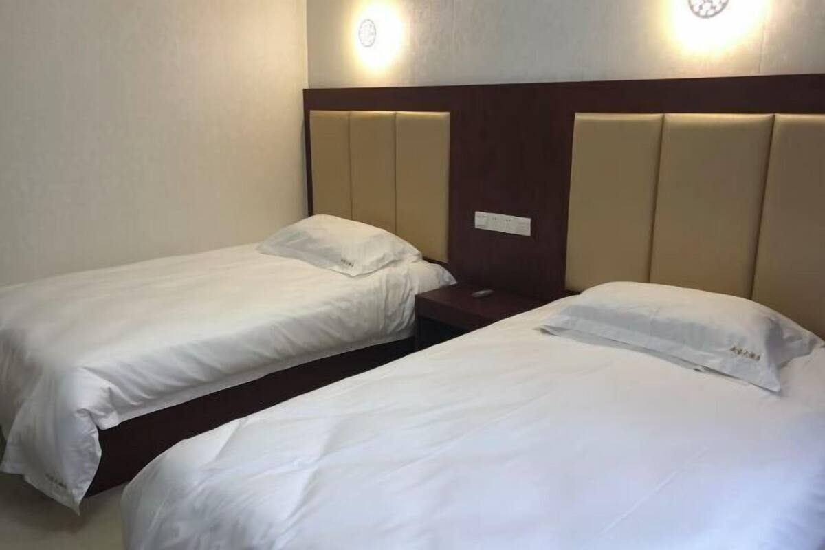 A hotel room with two single beds, each with white bedding and headboards.
