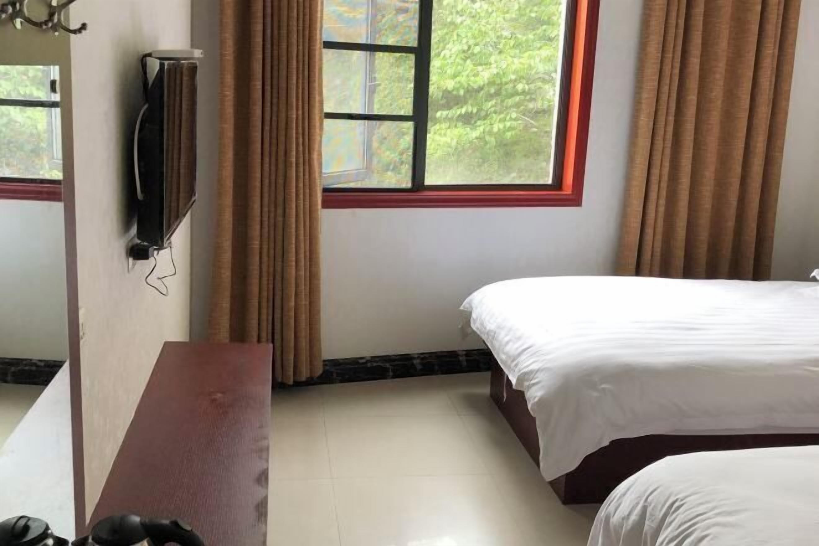 Habitación de hotel con dos camas, un televisor montado en la pared y una ventana con cortinas.