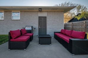 Une terrasse avec deux canapés en osier, un barbecue et une porte.