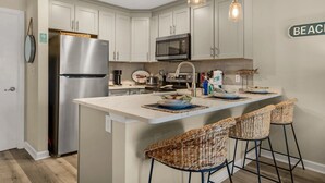 A modern kitchen with white cabinets, stainless steel appliances, a central island with bar stools, and a sign reading "BEACH".