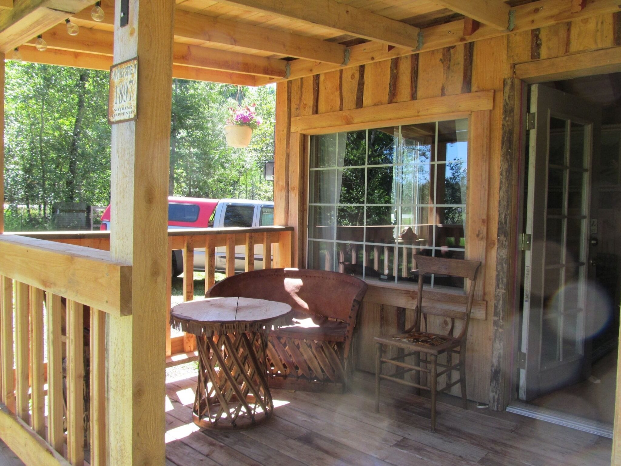 A wooden deck with a table and chairs, a hanging flower pot, and a view of the outside.