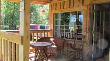 A wooden deck with a table and chairs, a hanging flower pot, and a view of the outside.