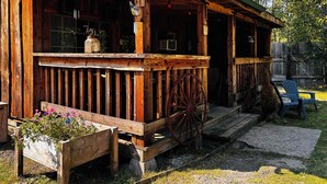 A rustic wooden cabin with a porch, a welcome sign, a vintage wagon wheel, and a planter with flowers.