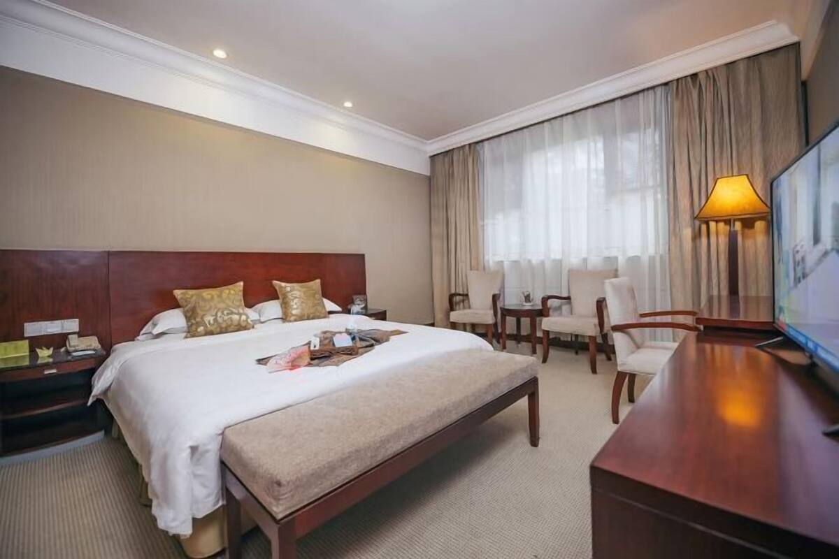Ein Hotelzimmer mit einem großen Bett, einem Schreibtisch, einem Stuhl und einem Fernseher.