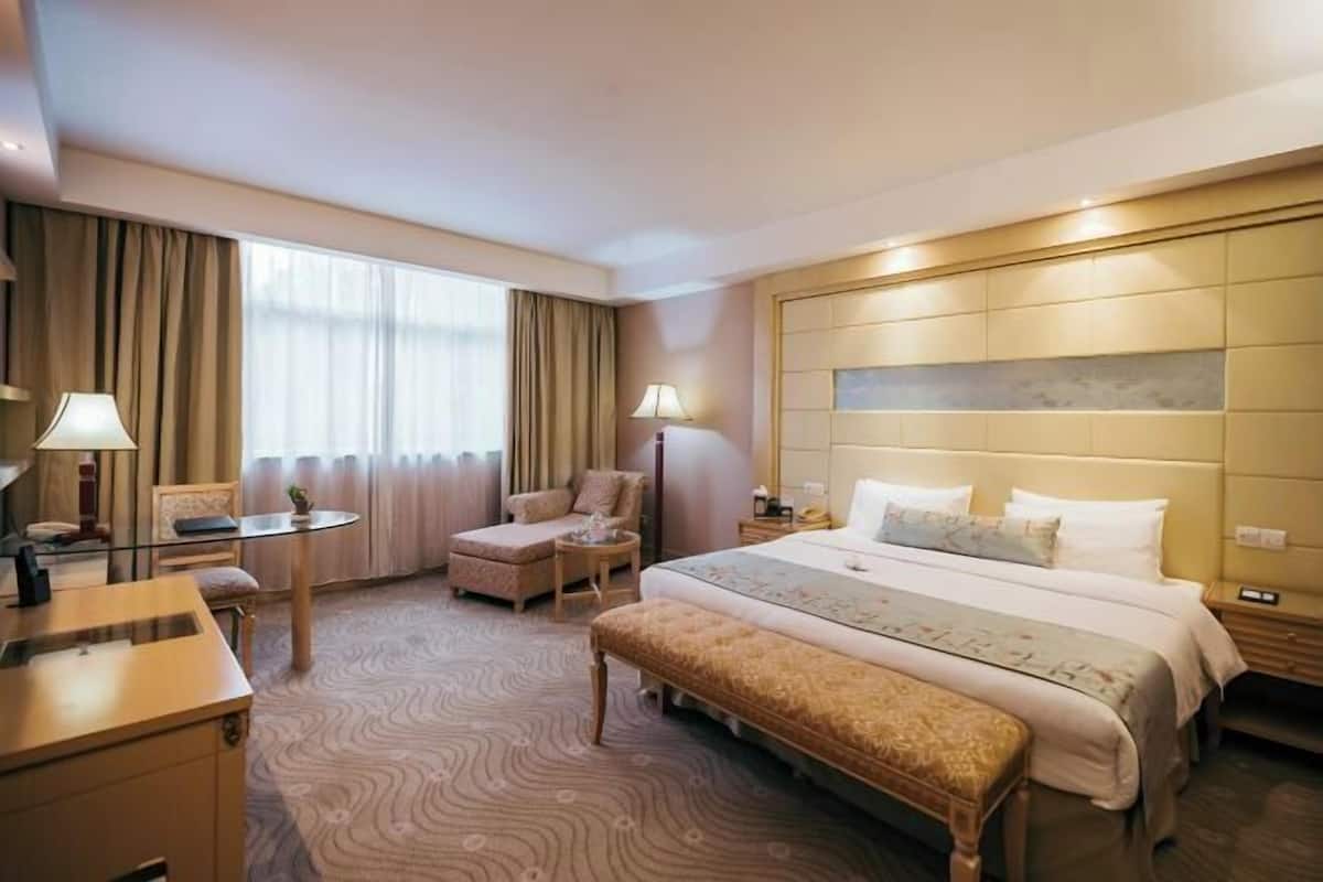 Ein Hotelzimmer mit Bett, Schreibtisch, Stuhl, kleinem Tisch und Bank.
