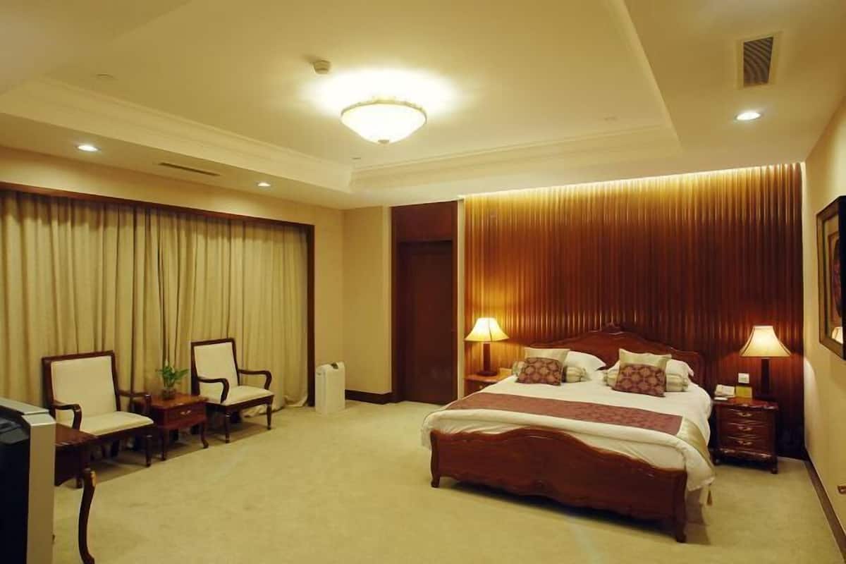 Ein Hotelzimmer mit einem großen Bett, zwei Nachttischen mit Lampen, einem Schreibtisch mit Stuhl und einem großen Fenster mit Vorhängen.