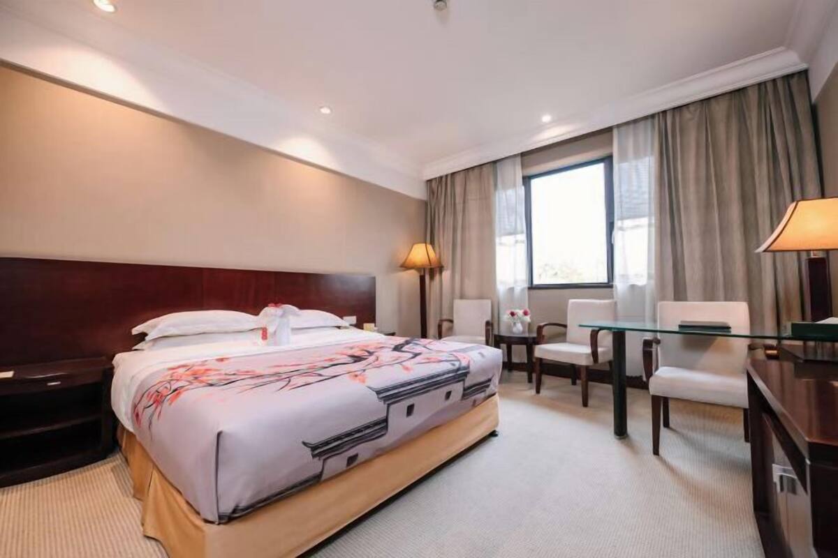 Ein Hotelzimmer mit einem großen Bett, einem Schreibtisch, einem Sessel und einer Aussicht auf die Stadt durch das Fenster.