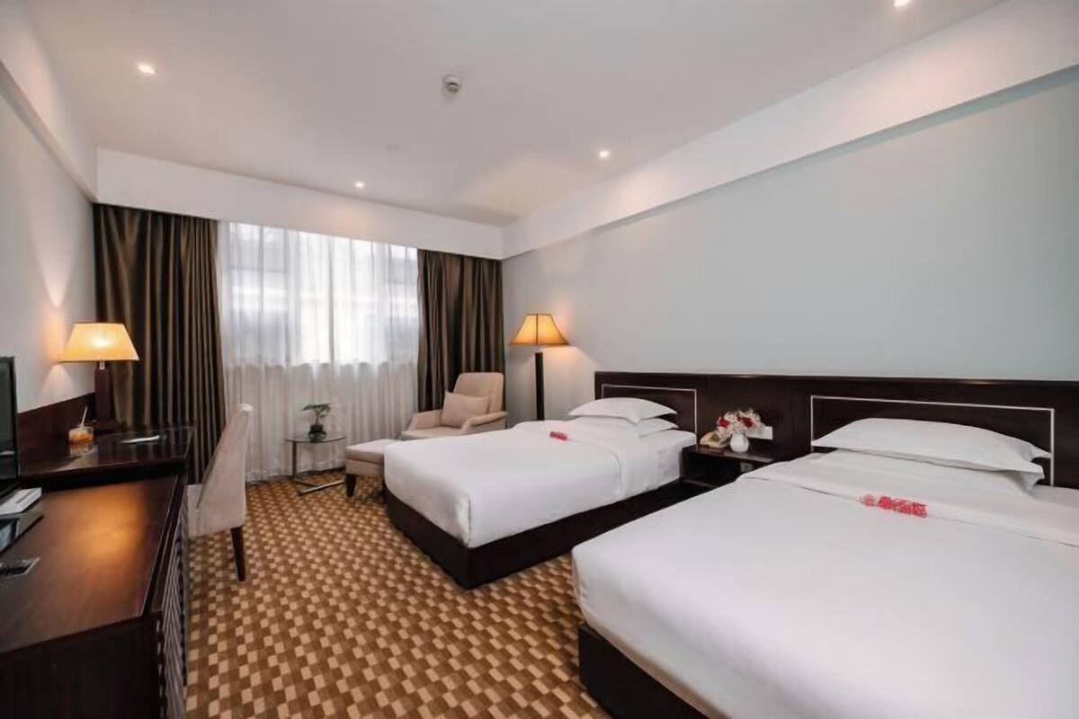 Ein Hotelzimmer mit zwei Betten, einem Schreibtisch, einem Stuhl und einem kleinen Tisch mit einer Lampe.