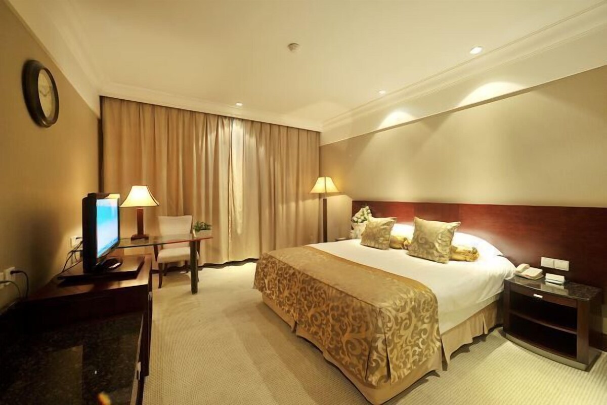 Habitación de hotel con una cama grande, dos lámparas de noche, un escritorio con una computadora, una silla y un reloj en la pared.