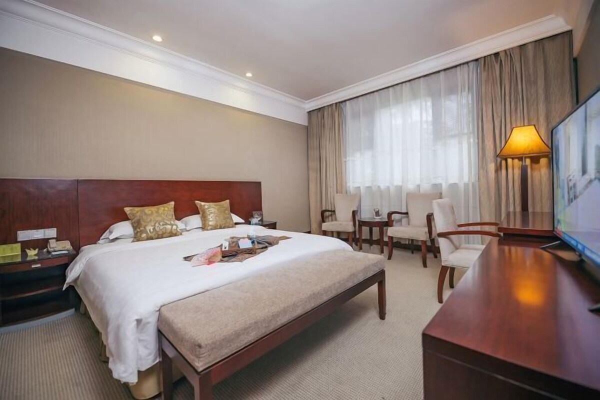 Una habitación de hotel con una cama grande, un escritorio, una silla, un televisor y una ventana con cortinas.
