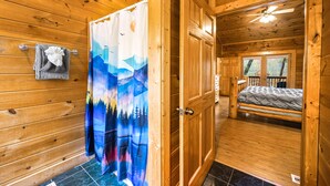A wooden cabin interior with a bed, a shower curtain with a forest scene, and a window with a view of trees. - Fall Break Special!•Hot Tub•Game Room•Sleeps 22•3600 sq ft •Pigeon Forge (Pigeon Forge)