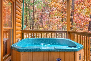 Un jacuzzi en una terraza de madera con vistas a árboles otoñales.