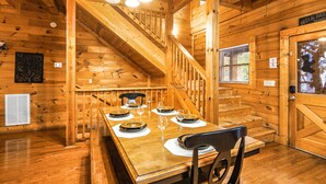 A wooden cabin interior with a dining table set for four, a staircase, and a bed & breakfast sign. - Fall Break Special!•Hot Tub•Game Room•Sleeps 22•3600 sq ft •Pigeon Forge (Pigeon Forge)