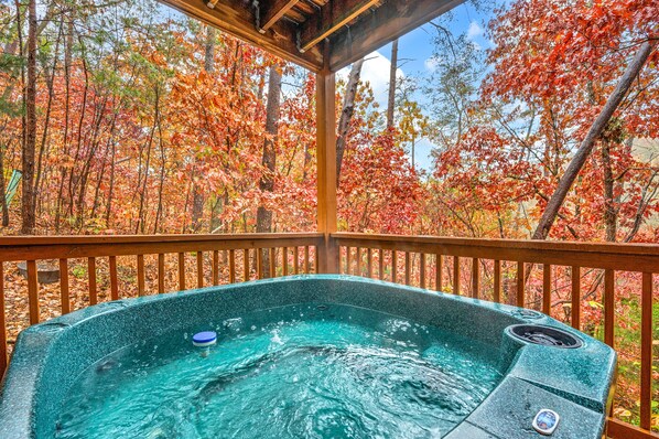 Un jacuzzi en una terraza de madera con vistas a árboles otoñales.