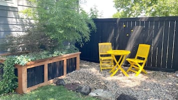 A garden area with a wooden planter, yellow chairs, and a black fence.