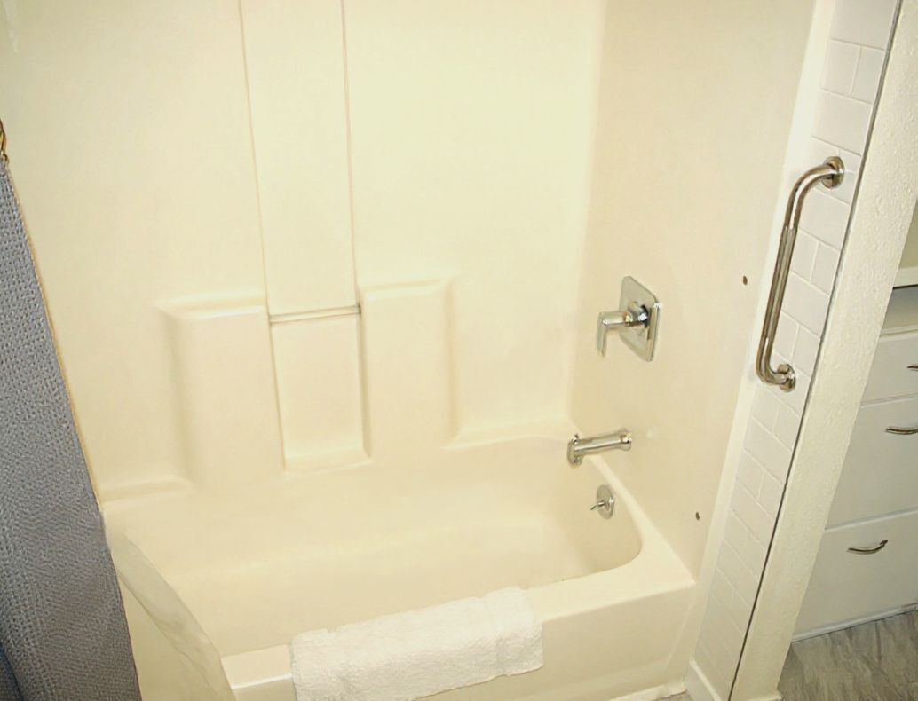 A bathtub with a towel, a grab bar, and a white tiled wall.