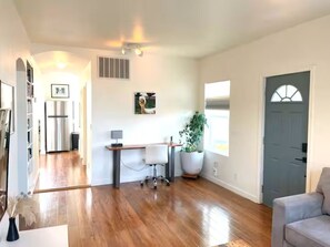 A spacious living area with hardwood flooring, a white couch, a desk with a chair, a potted plant, and a grey door. - Crofty Cottage Dog-Approved Boise Bench Charmer with Private Fenced Yard (Boise)