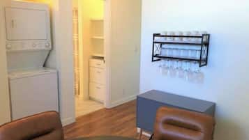 A compact living space with a laundry area, a dining table with chairs, and a wall-mounted glass storage unit.